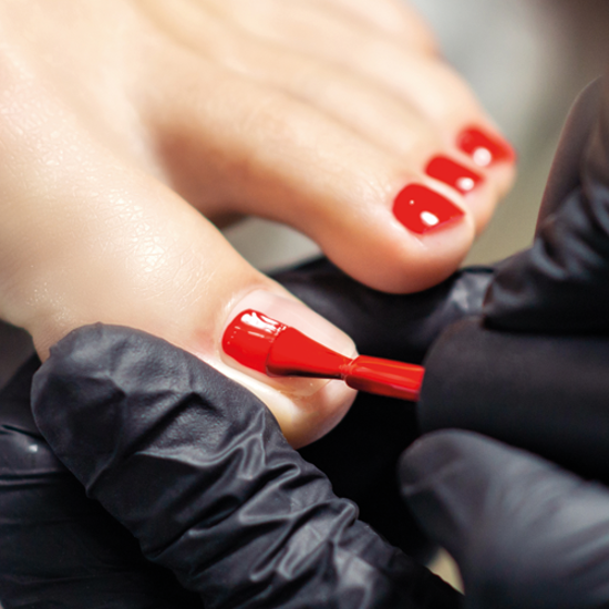 Fußpflege-Behandlung an den Zehennägeln mit rotem Nagellack.